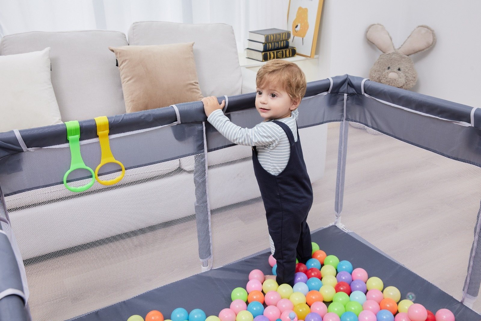 Toddler pulling up on the rings of an Orian Babies playpen in a living room